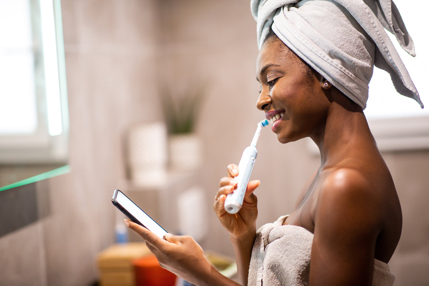 A woman brushing her teeth at home in a bright bathroom.
