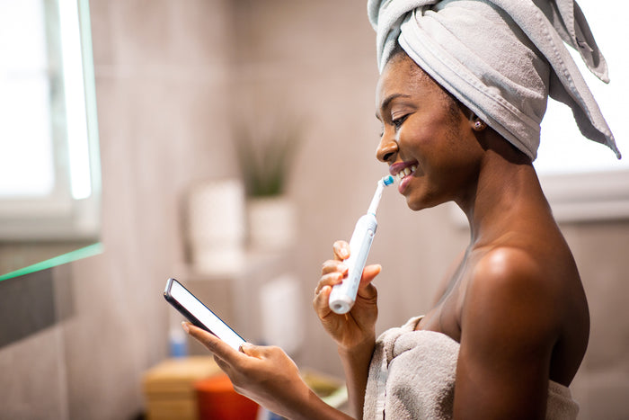 A woman brushing her teeth at home in a bright bathroom.