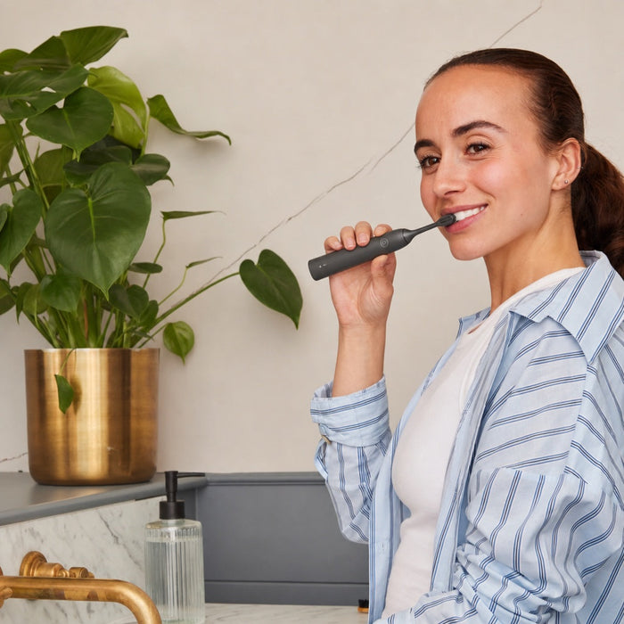 A woman brushing her teeth with an electric toothbrush as part of her daily routine