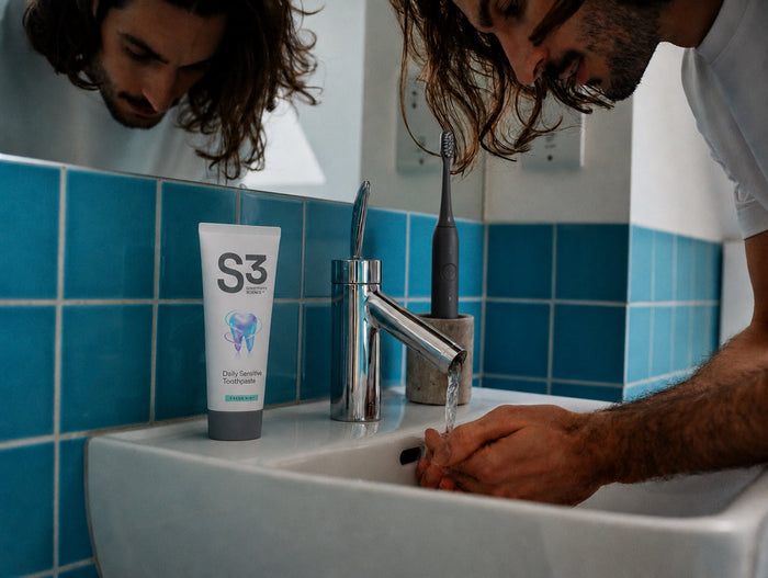 A man rinsing at a bathroom sink with a tube of S3 Daily Sensitive Toothpaste on the basin
